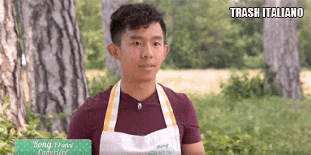 a young man wearing an apron is standing in a field with trees in the background and a sign that says trash italiano