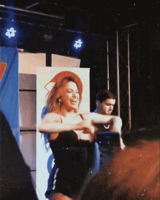 a woman in a black dress is dancing on a stage while a man takes a picture of her