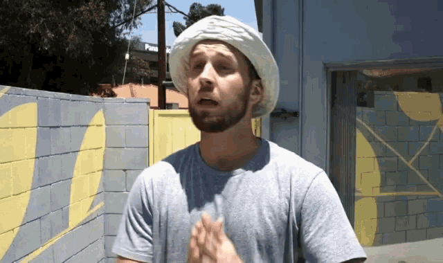a man wearing a white hat and a grey shirt is standing in front of a brick wall