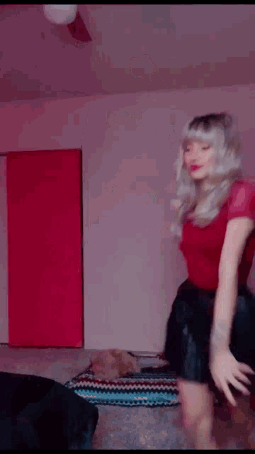 a woman in a red shirt and a black skirt is dancing in a room .