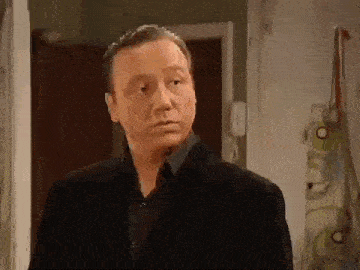 a man in a black suit is standing in front of a door looking at the camera .