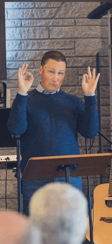 a man in a blue sweater is giving a ok sign