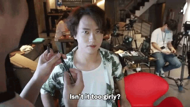 a woman is applying makeup to a young man 's face and asking if it is too girly