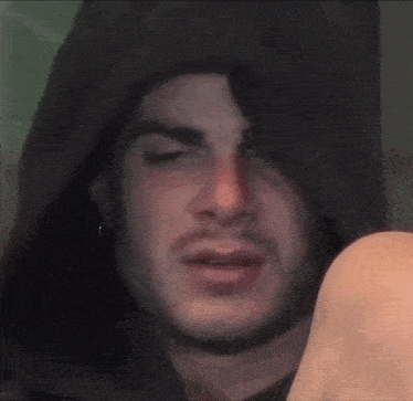 a man with a beard is wearing a black hooded jacket and making a funny face .