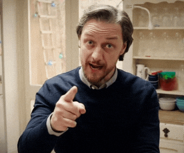 a man in a blue sweater is pointing his finger at the camera