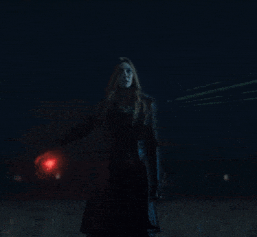 a woman in a red dress is standing in a field with a red light behind her