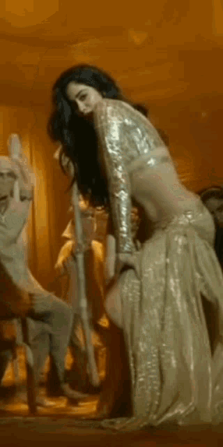 a woman in a gold dress is dancing in front of a group of people .
