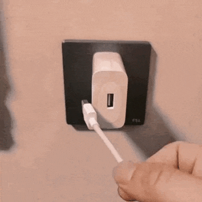 a person is plugging a charging cable into a wall socket .