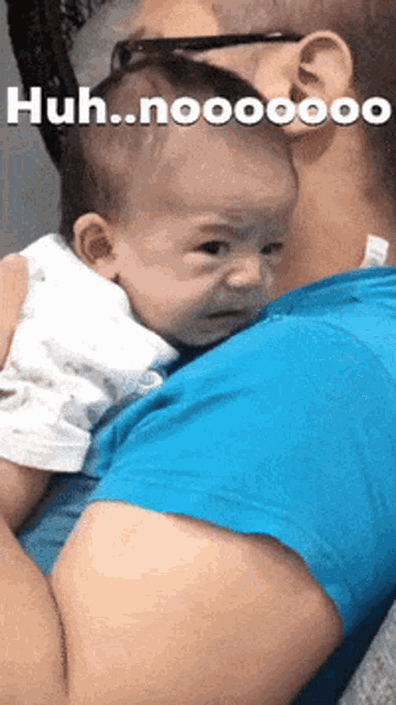 a man is holding a crying baby in his arms and the baby is making a face