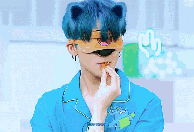 a person with blue hair is wearing a cat mask and eating a cookie