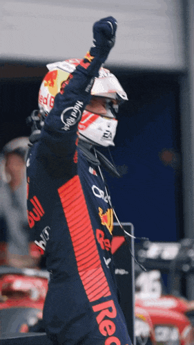 a man wearing a helmet and a red bull outfit holds his fist in the air