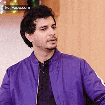 a man wearing a purple jacket and a black shirt is looking at the camera .