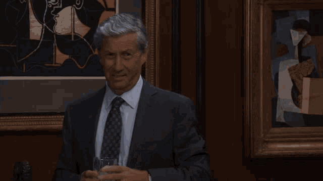 a man in a suit and tie drinking from a glass in front of a painting