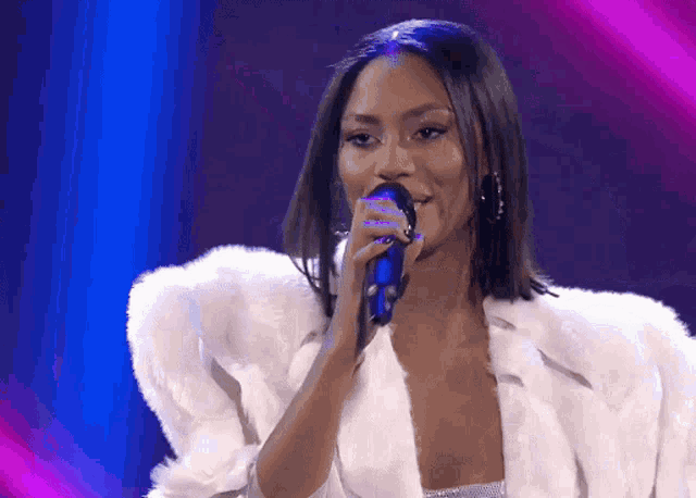 a woman is singing into a microphone while wearing a fur coat