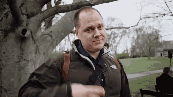 a man wearing a north face jacket is standing in front of a tree in a park .