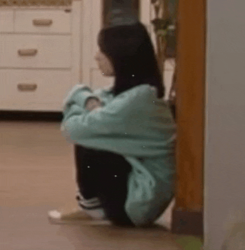 a woman is sitting on the floor in a kitchen with her legs crossed .