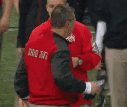 a man in a red nike jacket is talking to another man in a green shirt .