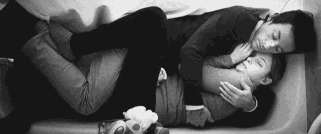 a man and a woman are laying in a bathtub hugging .