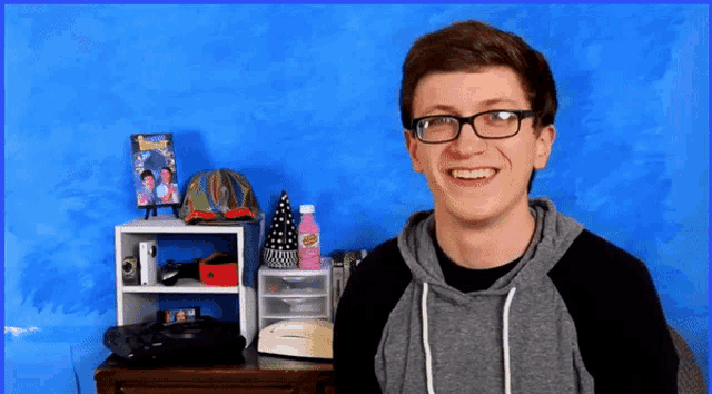 a young man wearing glasses is smiling in front of a blue background