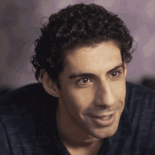 a man with curly hair and a blue shirt smiles for the camera