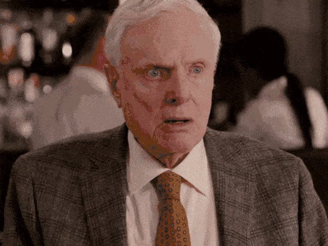 an older man wearing a suit and tie is making a surprised face