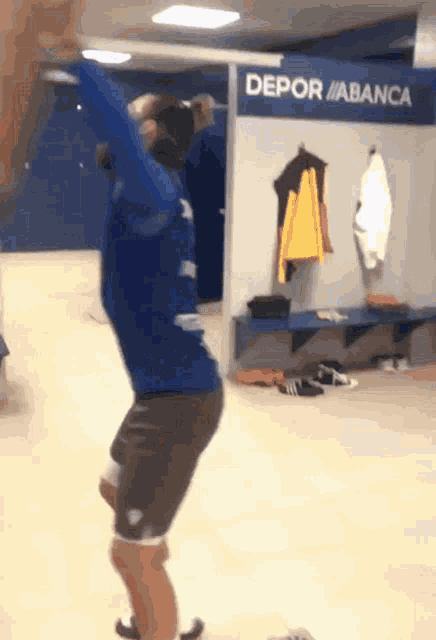 a man in a blue shirt is dancing in a locker room with a sign that says depor abanca