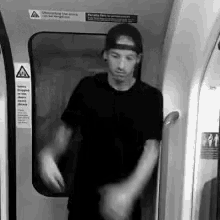 a man wearing a baseball cap and a black shirt is standing in a train car .