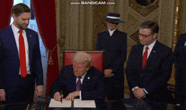 a man in a suit and tie is signing a document while another man watches