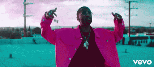 a man in a pink jacket is standing on a roof with his arms outstretched .