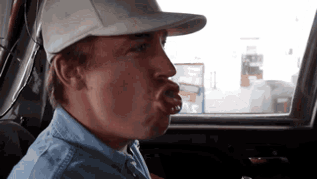 a man wearing a hat and a blue shirt is sticking his tongue out in a car