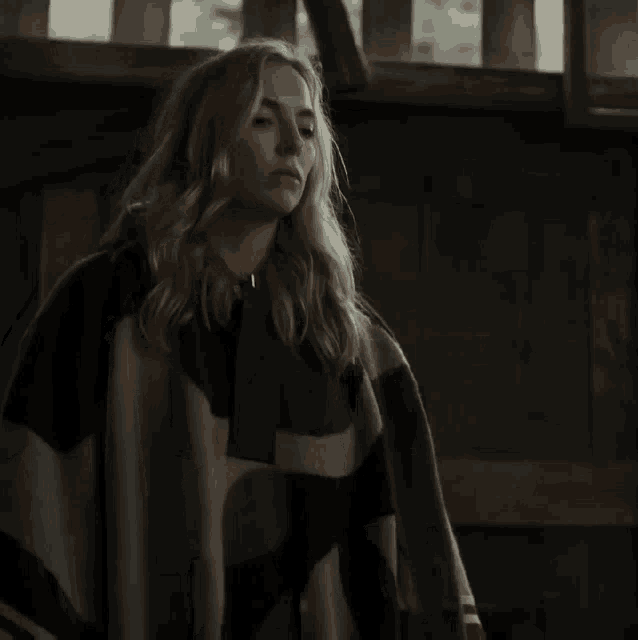 a woman wearing a plaid poncho is standing in a dark room