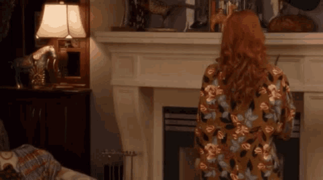 a woman in a floral dress is standing in front of a fireplace in a living room .