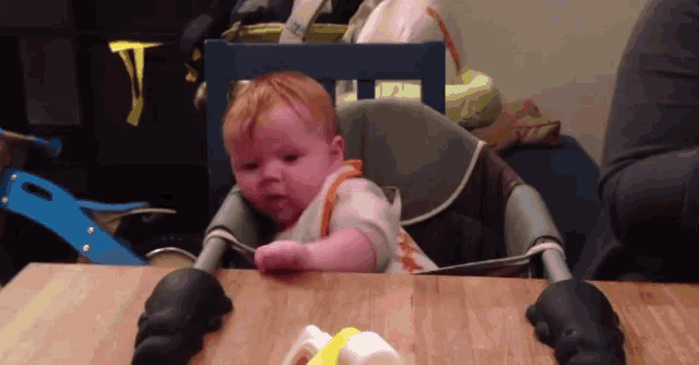 a baby is sitting in a high chair looking at something on the table