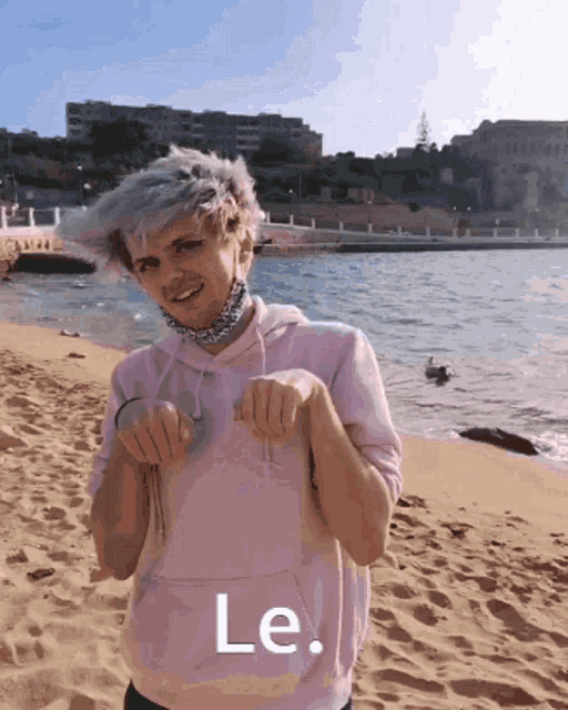 a man in a pink hoodie is standing on a sandy beach with the word le written on the bottom