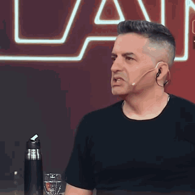 a man wearing a black shirt and ear buds is sitting in front of a sign that says la