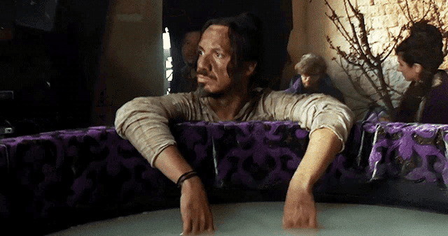 a man with a beard is sitting in a bathtub with purple cushions