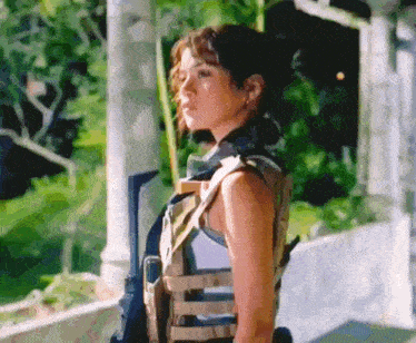 a woman wearing a military vest and holding a gun is standing in front of a building .