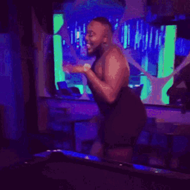 a man without a shirt is dancing in a dark room with purple lights
