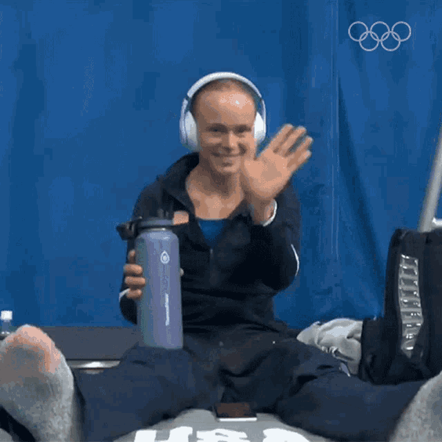 a woman wearing headphones is holding a purple water bottle and waving