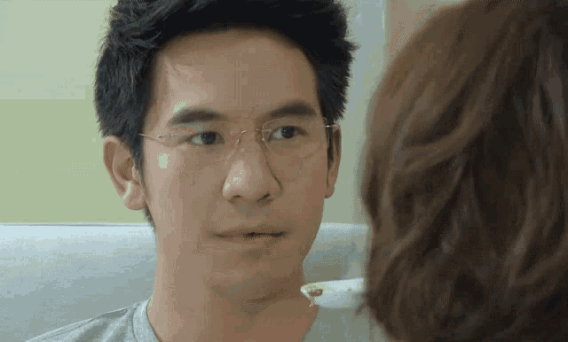a man wearing glasses looks at a woman holding a spoon