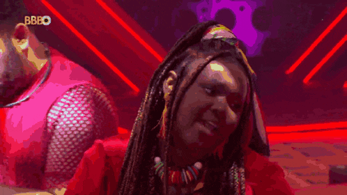 a woman with braids and a necklace is smiling in front of a red background with bbbo written on it