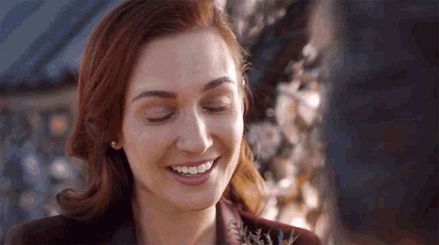 a woman with red hair is smiling with her eyes closed in front of flowers