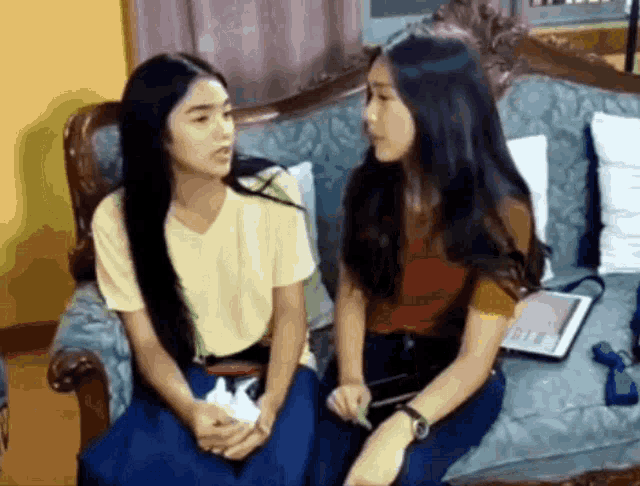 two young girls are sitting on a couch talking to each other .