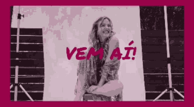 a woman is sitting on a chair in front of a pink background with the word vem aí written on it .