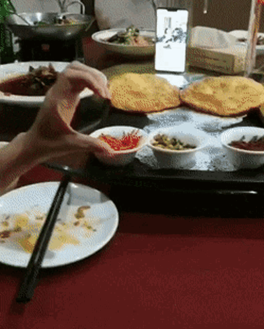 a person reaches for a bowl of food on a table with plates and chopsticks