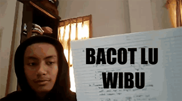 a man in a hoodie holds up a piece of paper that says bacot lu wibu