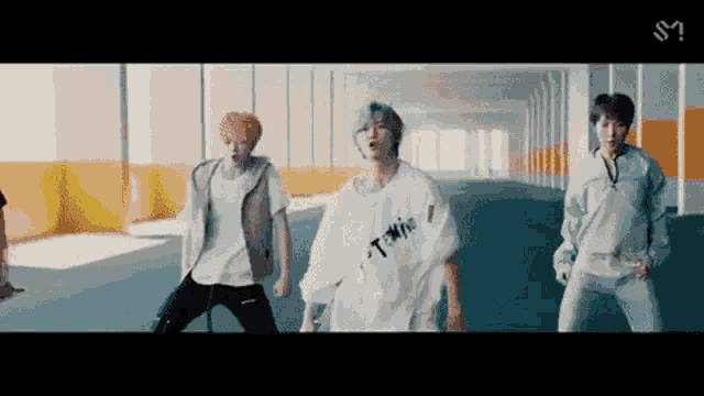 a group of young men are dancing in a hallway with the letter m on the bottom right
