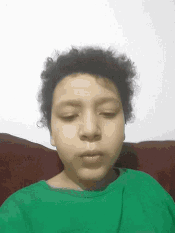 a young boy with curly hair is wearing a green shirt and sleeping with his eyes closed
