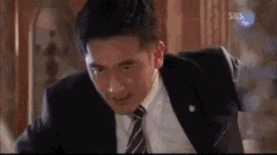 a man in a suit and tie is sitting at a table and making a funny face .