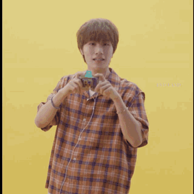 a man in a plaid shirt is taking a picture with a yellow background and the words byd land below him